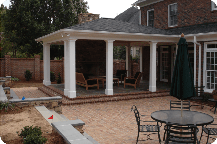 Brick house with a covered porch featuring a fireplace and seating area, adjacent to a patio with outdoor furniture.