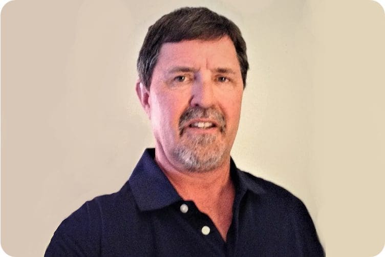 Man with a mustache wearing a dark polo shirt against a light background.